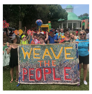 A group of people walking with a hand painted banner that reads: Weave The People